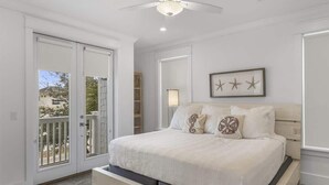 A bedroom with a bed, a ceiling fan, a window with a view, and a door leading to a balcony.