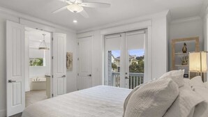 A bedroom with a large bed, a ceiling fan, and a view of the outside.