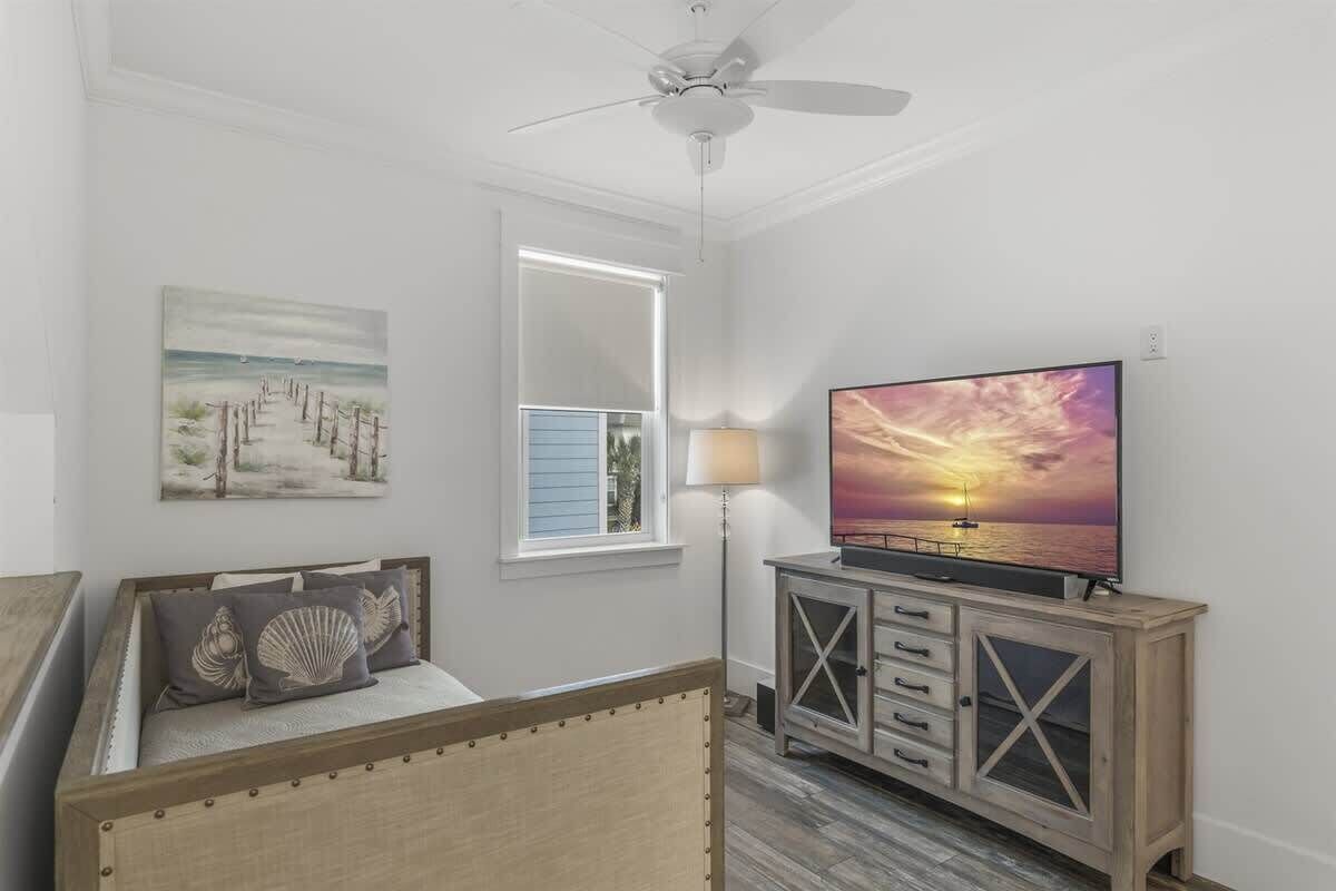 Un dormitorio con cama, televisor, ventilador de techo, ventana y un cuadro.