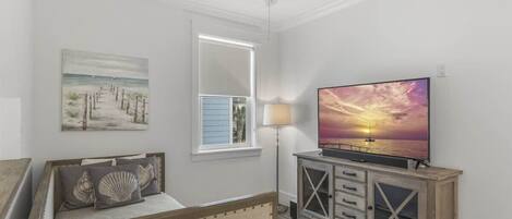 Un dormitorio con cama, televisor, ventilador de techo, ventana y un cuadro.