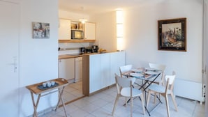 A compact kitchen with white cabinets, a microwave, and a coffee machine. There is a dining table with four chairs and a small side table with cups. - Domaine de Clairefontaine by Interhome (Deauville-Trouville)