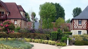 A residential area with traditional half-timbered houses, a well-maintained garden with various shrubs and flowers, and a curved pathway. - Domaine de Clairefontaine by Interhome (Deauville-Trouville)