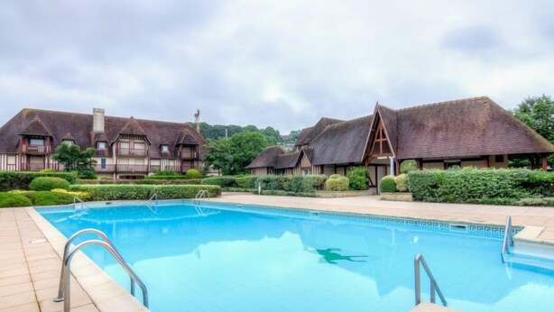 A swimming pool with a tiled deck, surrounded by traditional buildings with thatched roofs. - Domaine de Clairefontaine by Interhome (Deauville-Trouville)