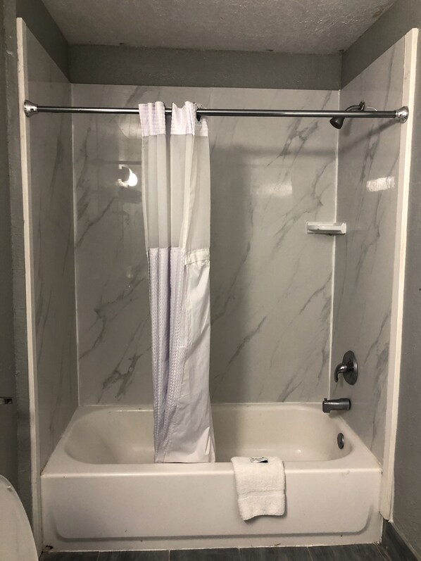 A bathroom with a white bathtub, a shower curtain, and a marble wall.