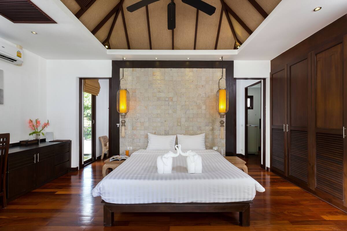 A spacious bedroom with a large bed, wooden ceiling, and a stone wall.