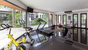 Un gimnasio moderno con cintas de correr, una bicicleta estática y equipo de pesas. Amplias ventanas ofrecen vistas al exterior.