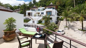 Un hotel moderno con balcón, sillones de descanso verdes y una planta grande en maceta.