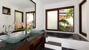 Un baño moderno con dos lavamanos de vidrio, un espejo grande y vistas a un jardín tropical.