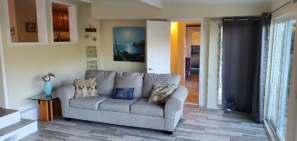 A living room with a grey sofa, a small table with a vase, and a painting on the wall.