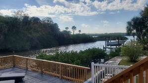 Une terrasse en bois avec des chaises longues donnant sur une rivière, entourée d’une végétation luxuriante et avec un quai visible au loin.