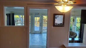 Un couloir avec un ventilateur de plafond, une porte donnant sur l’extérieur et un miroir accroché au mur.