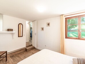 Un dormitorio con cama, una silla de madera, una mesita, un espejo y una ventana con cortinas.