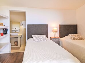 Two single beds with matching headboards and pillows, a bedside table and lamp, and a shelf with books and decorative items.