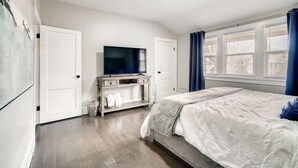 Une chambre à coucher avec un lit, un téléviseur posé sur un meuble et une fenêtre avec des rideaux.