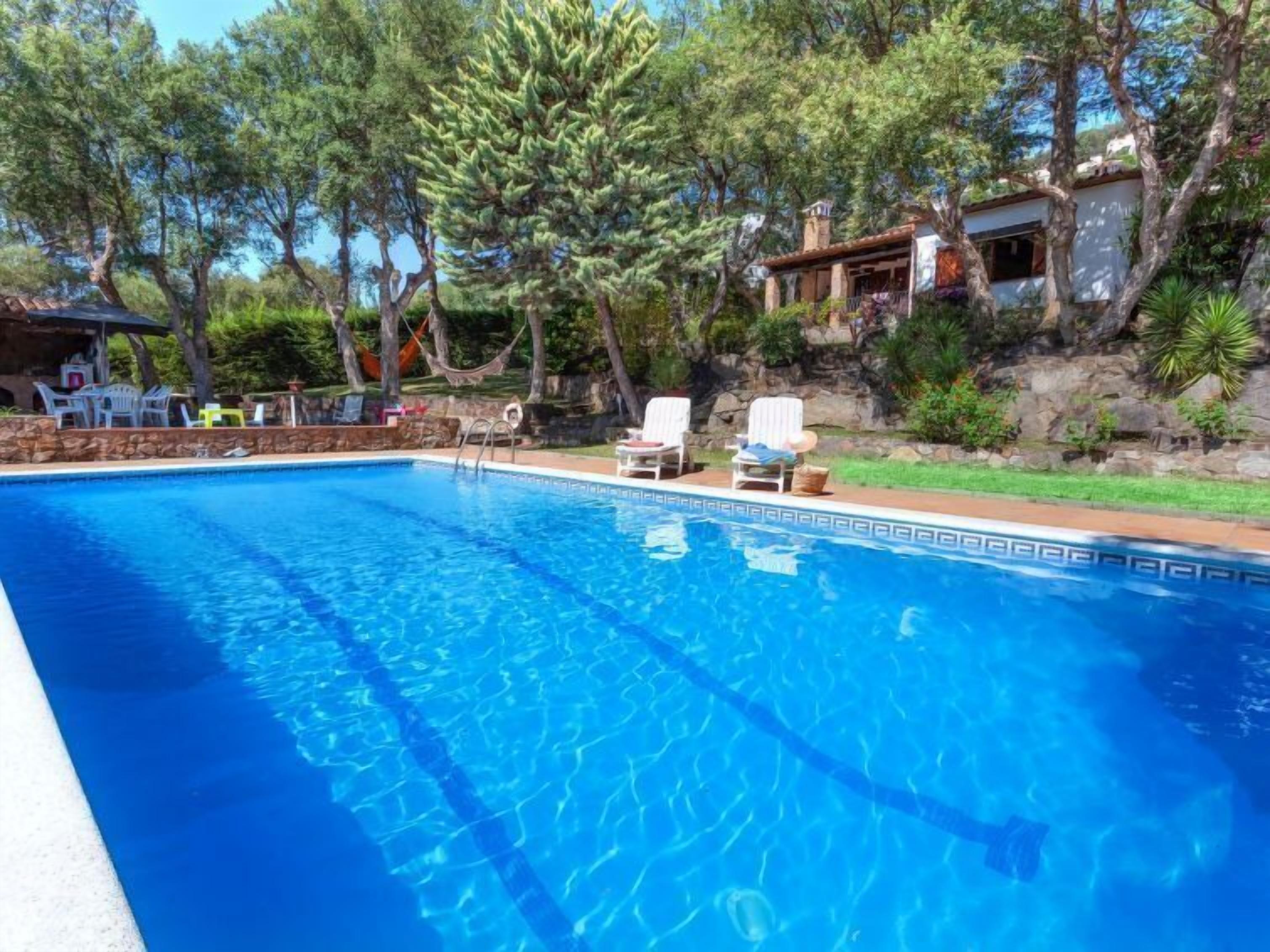 A clear blue swimming pool with lounge chairs and a stone wall.