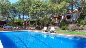 A clear blue swimming pool with lounge chairs and a stone wall. - La Plaza by Interhome (Calonge)