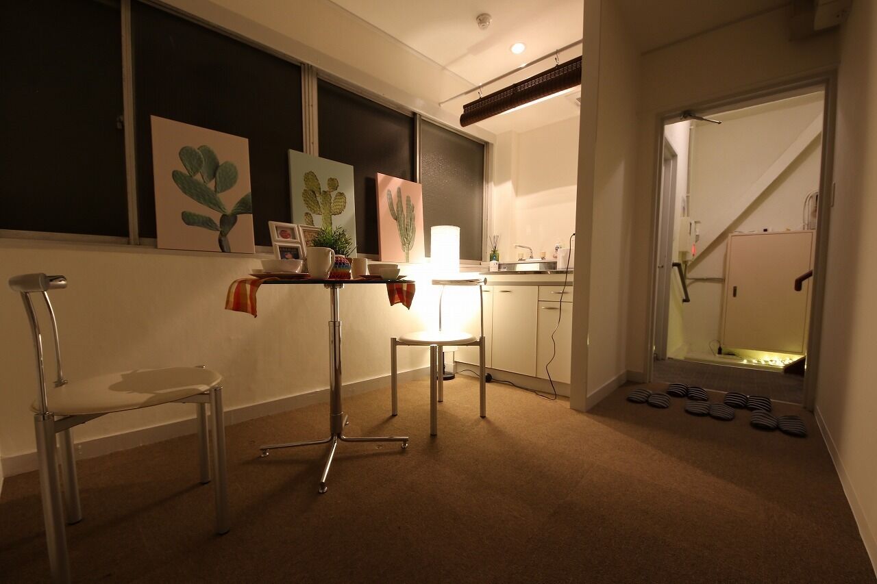 Une cuisine compacte avec un coin repas, comprenant une table avec des chaises, un petit meuble et une fenêtre décorée d’œuvres d’art.