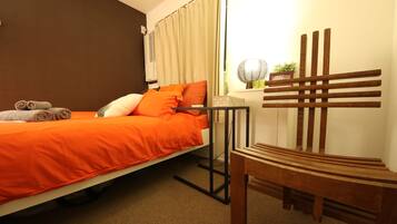 A bedroom with a bed, a chair, a bedside table, and a curtain.