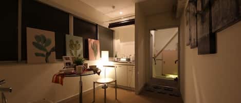A narrow hallway with a kitchenette on the right, a dining area with a table and chairs, and a staircase leading to another floor.