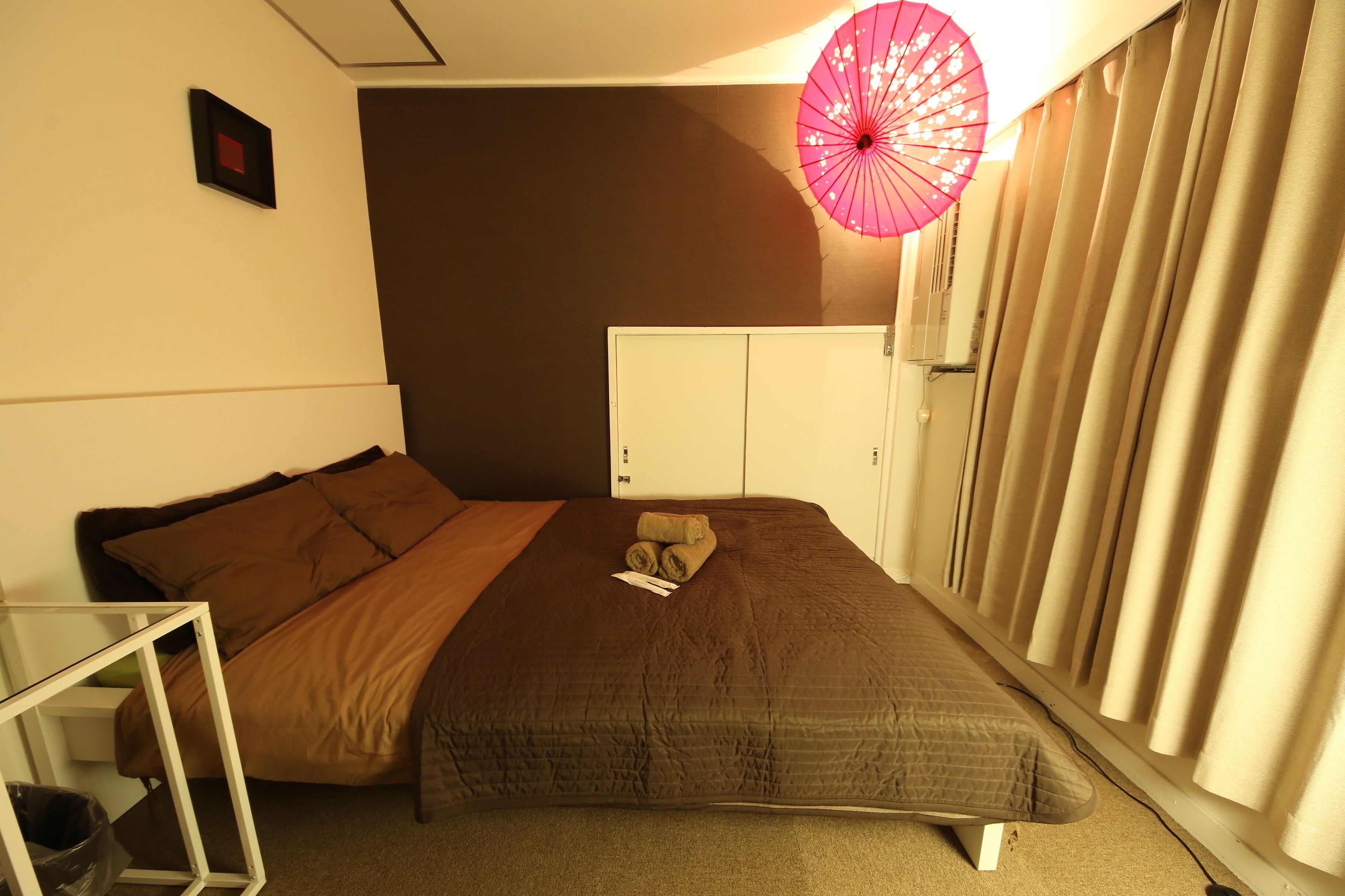 A bedroom with a bed, a small table, a wardrobe, and a window with curtains.