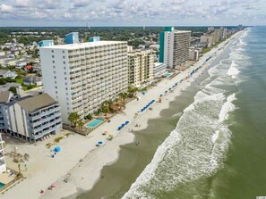 A beachfront hotel with multiple floors, a pool, and beach umbrellas.