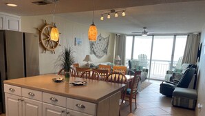 A spacious kitchen with a large island, wooden chairs, and a dining table. There is a view of a balcony with outdoor seating. - Direct Oceanfront 15th Floor Penthouse Views, 3 Bed 2.5 Bath Water's Edge Resort (Murrells Inlet)