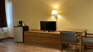 Een compacte kamer met een houten bureau, een televisie, een lamp, een koelkast en een stoel.