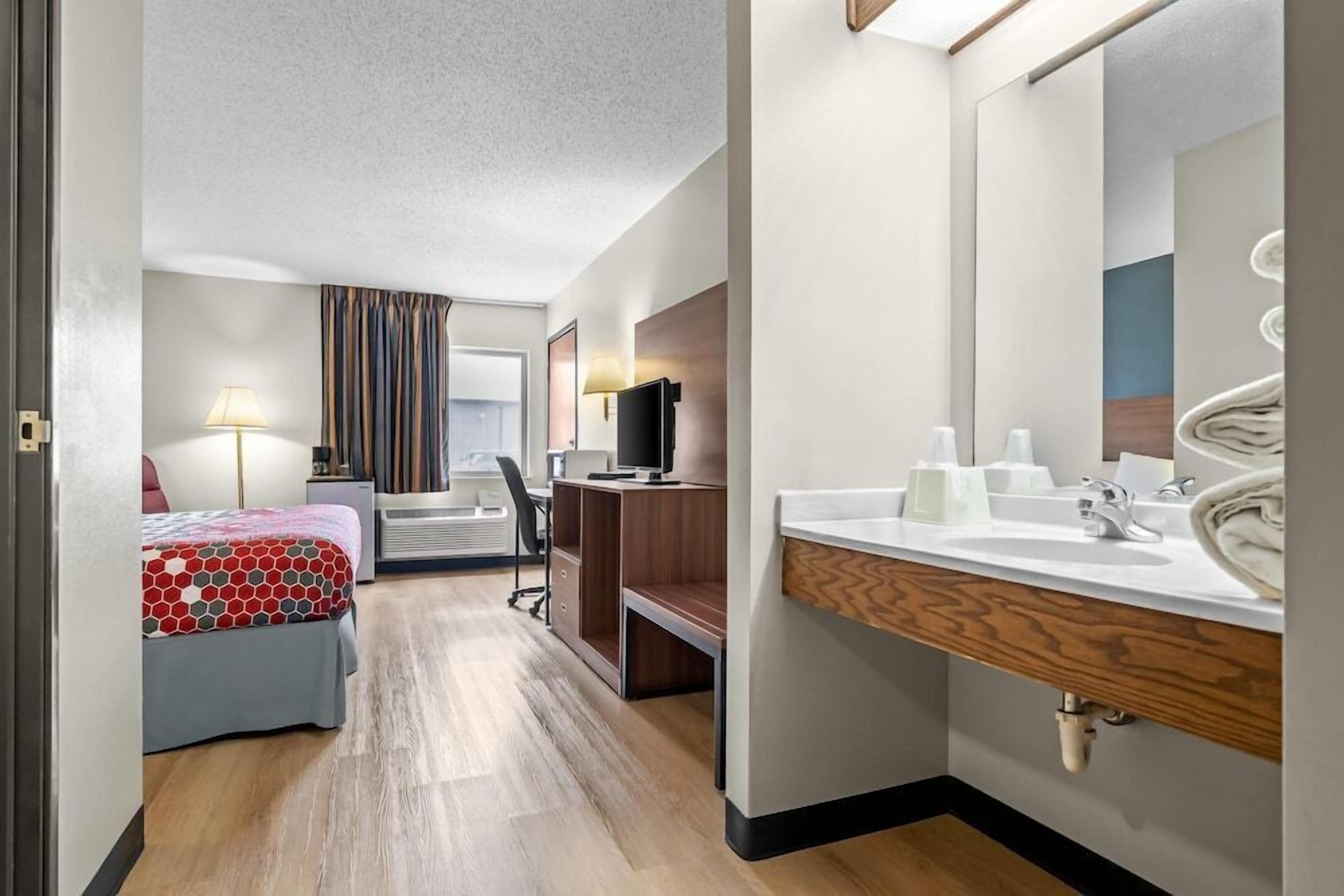 Habitación de hotel con cama, escritorio, silla y baño con lavamanos y espejo.