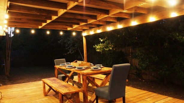 Une terrasse extérieure en bois, avec une table dressée pour le repas, entourée de chaises.