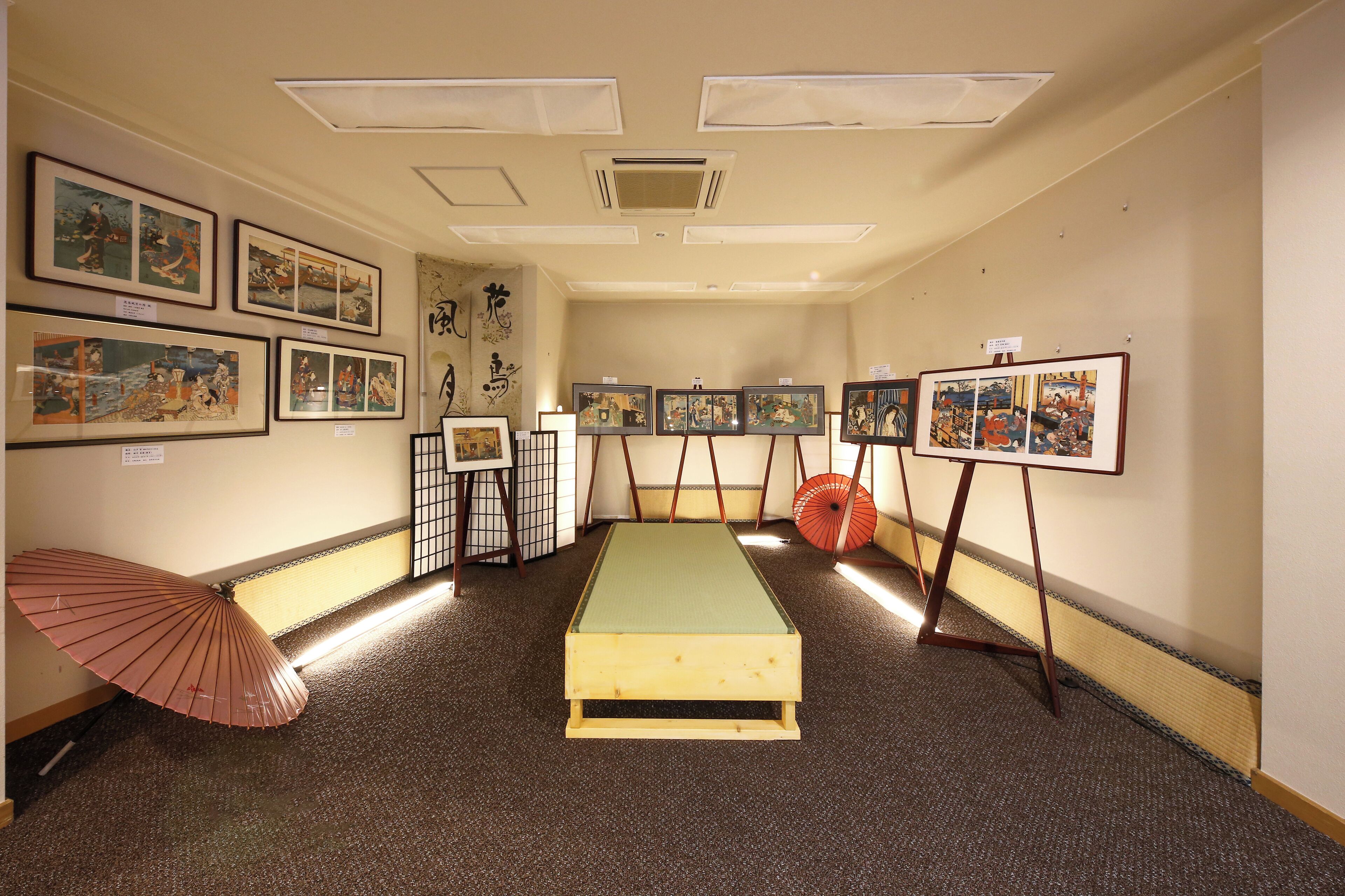 A room with a tatami mat, framed artworks on the walls, and a traditional Japanese folding fan.
