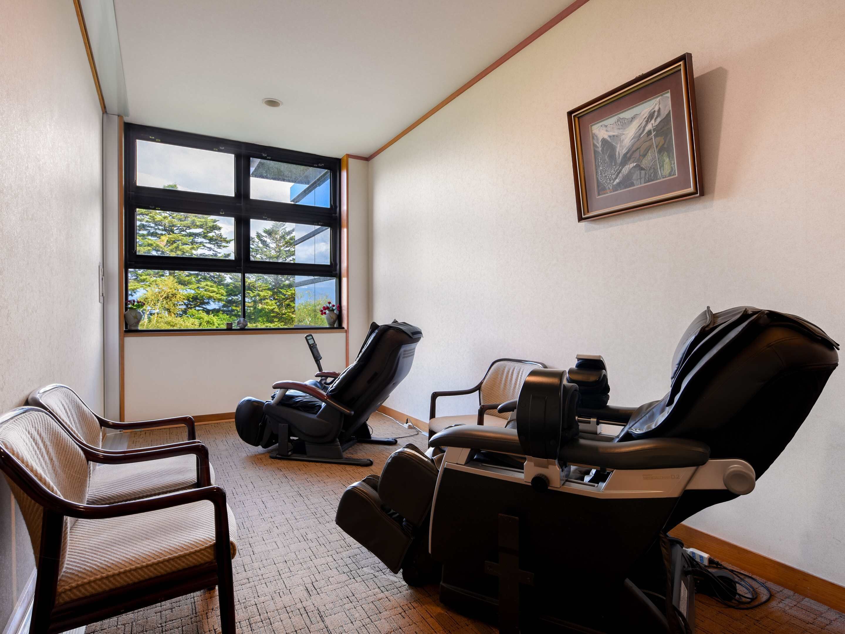 Un cuarto de terapia de masajes con dos camillas, una mesita pequeña y una ventana con vista a la vegetación.