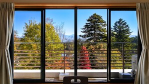 Una habitación con un ventanal amplio que da a un balcón con vistas a árboles y montañas.