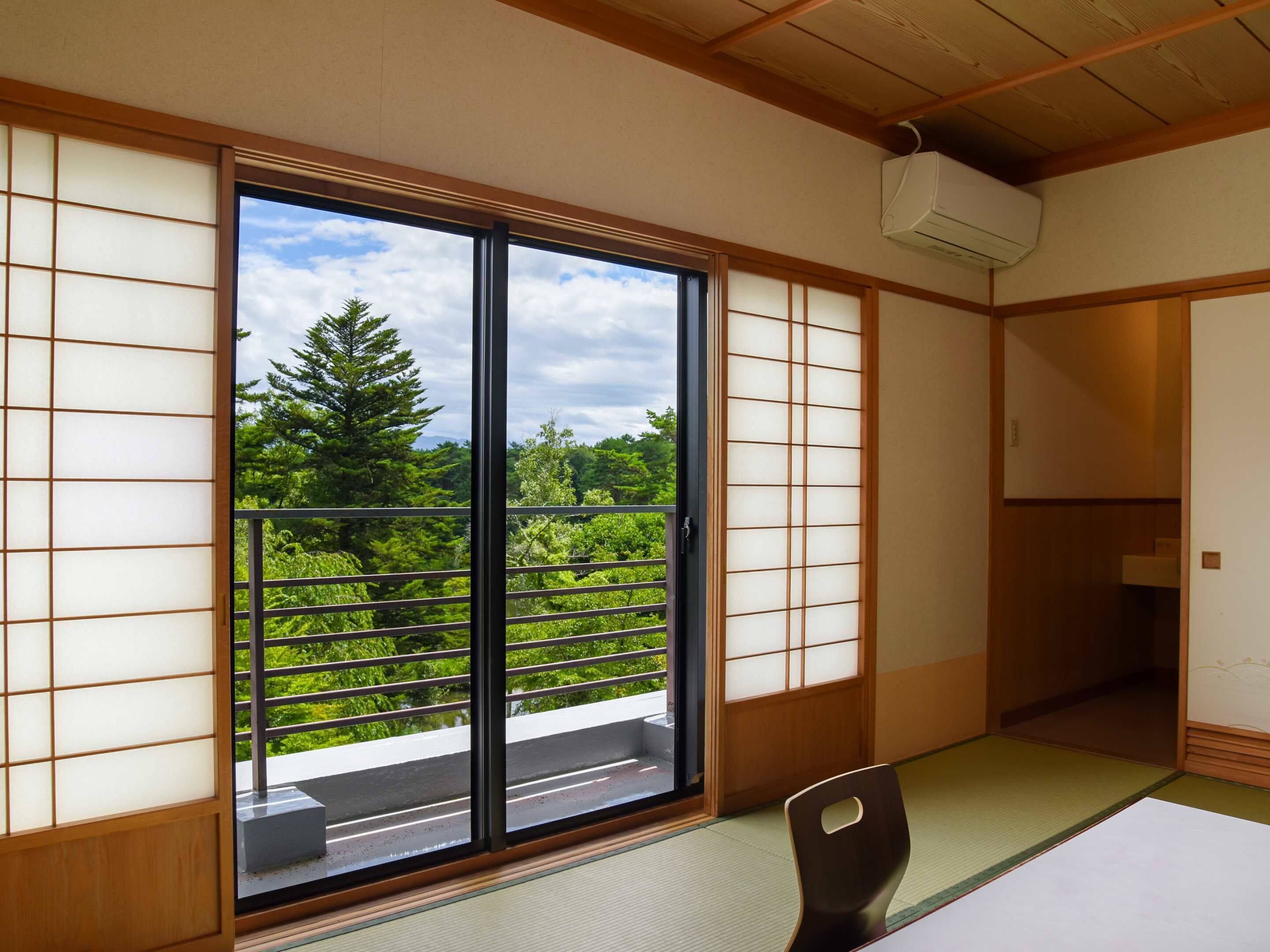 A traditional Japanese room with tatami flooring, a sliding door with a view of greenery, and a ceiling-mounted air conditioner.