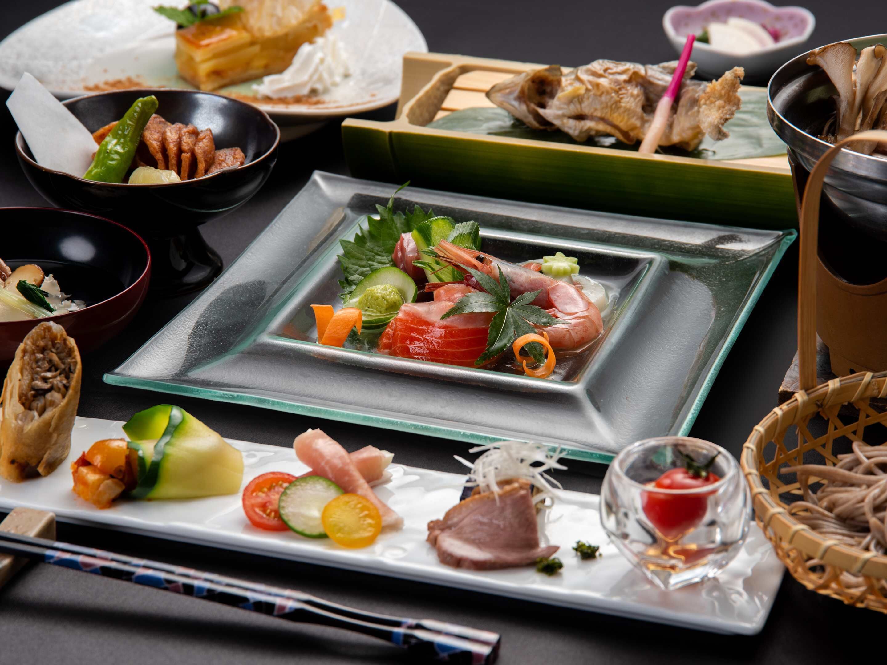 Variedad de platos, incluyendo sushi, sashimi y un tazón de sopa, dispuestos sobre una mesa junto a palillos y un vaso.