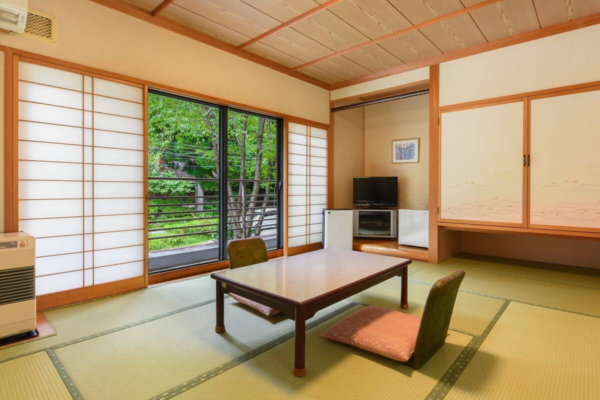 A traditional Japanese room with tatami flooring, a low table, chairs, sliding doors, and a television.