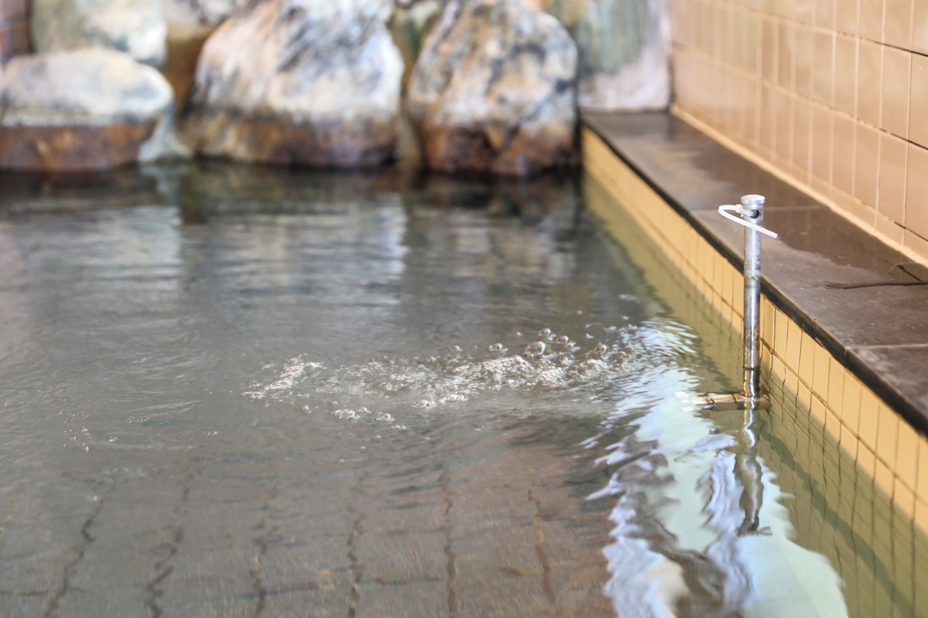 A pool with clear water, a metal pole, and tiled walls.