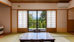 Una habitación japonesa tradicional con suelo de tatami, una puerta corredera con vistas a la vegetación y una mesa con sillas.