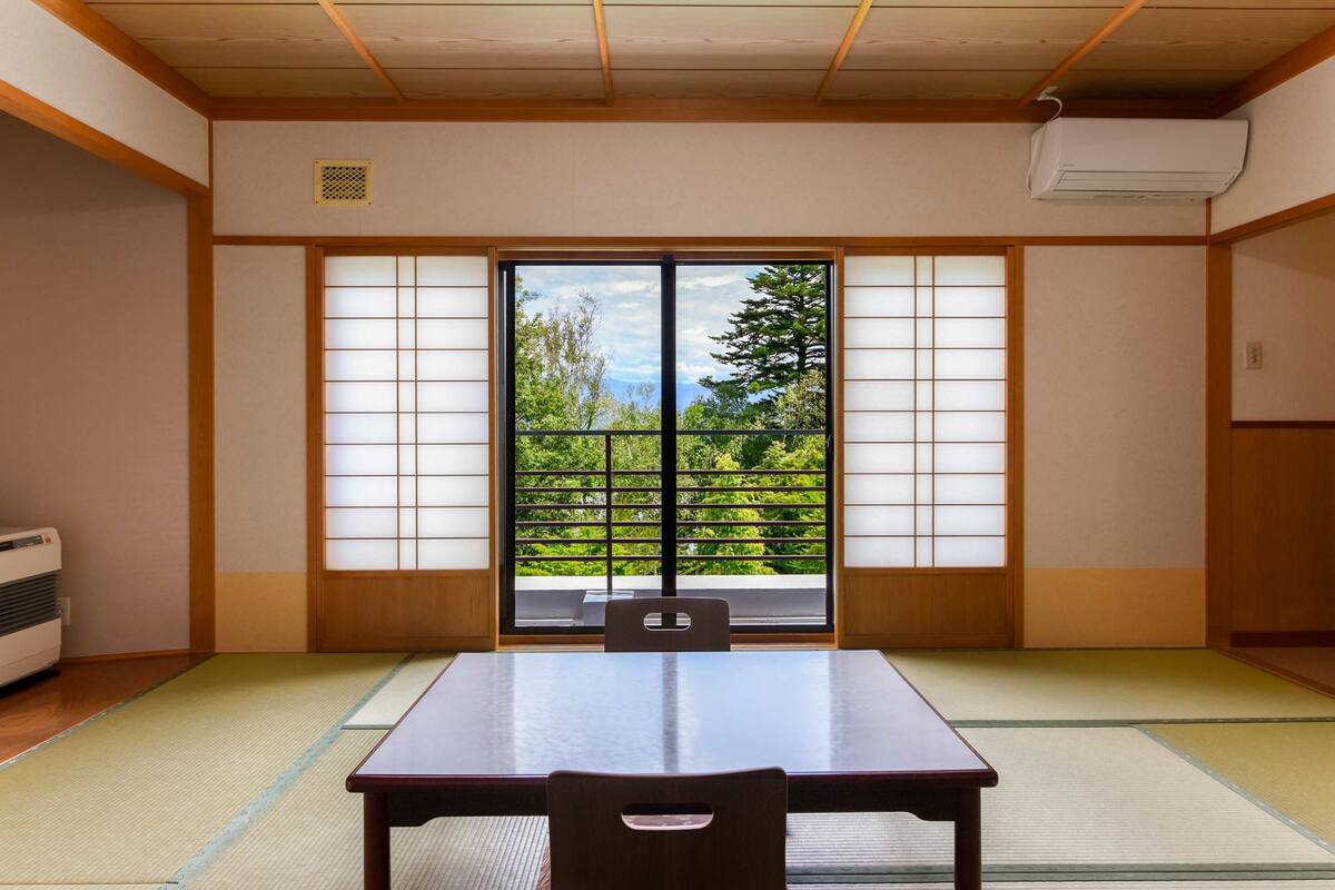 A traditional Japanese room with tatami flooring, a sliding door with a view of greenery, and a table with chairs.