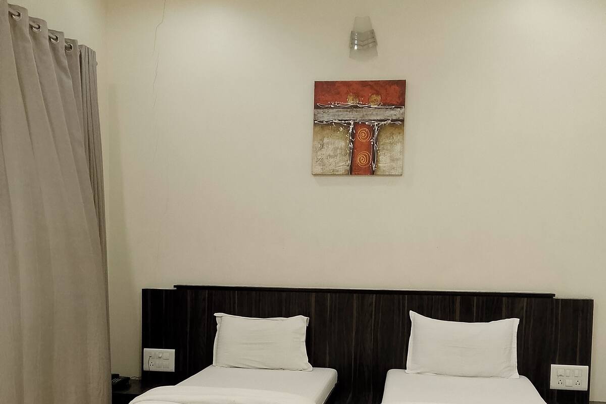 Ein Hotelzimmer mit zwei Betten, einem Bild an der Wand und einer Steckdose auf dem Nachttisch.