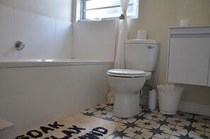 Een badkamer met een wit toilet, een badkuip en een betegelde vloer.