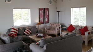 Ein geräumiges Wohnzimmer mit hoher Decke und freiliegenden Balken, ausgestattet mit einem grauen Sofagarnitur, einem Holztisch und einem gestreiften Sessel.