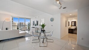 A modern living room with a glass dining table, white sofas, and a large window offering a city view. - Icon 2901 · ★ ICON BRICKELL-29th FLOOR OCEAN VIEWS-FREE SPA★ (Miami)