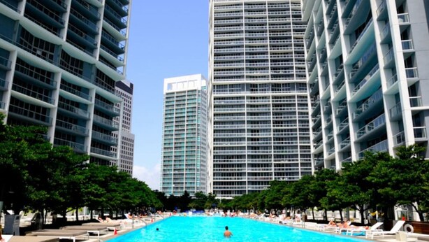 A large outdoor swimming pool surrounded by tall buildings, with lounge chairs and trees. - Icon 2901 · ★ ICON BRICKELL-29th FLOOR OCEAN VIEWS-FREE SPA★ (Miami)