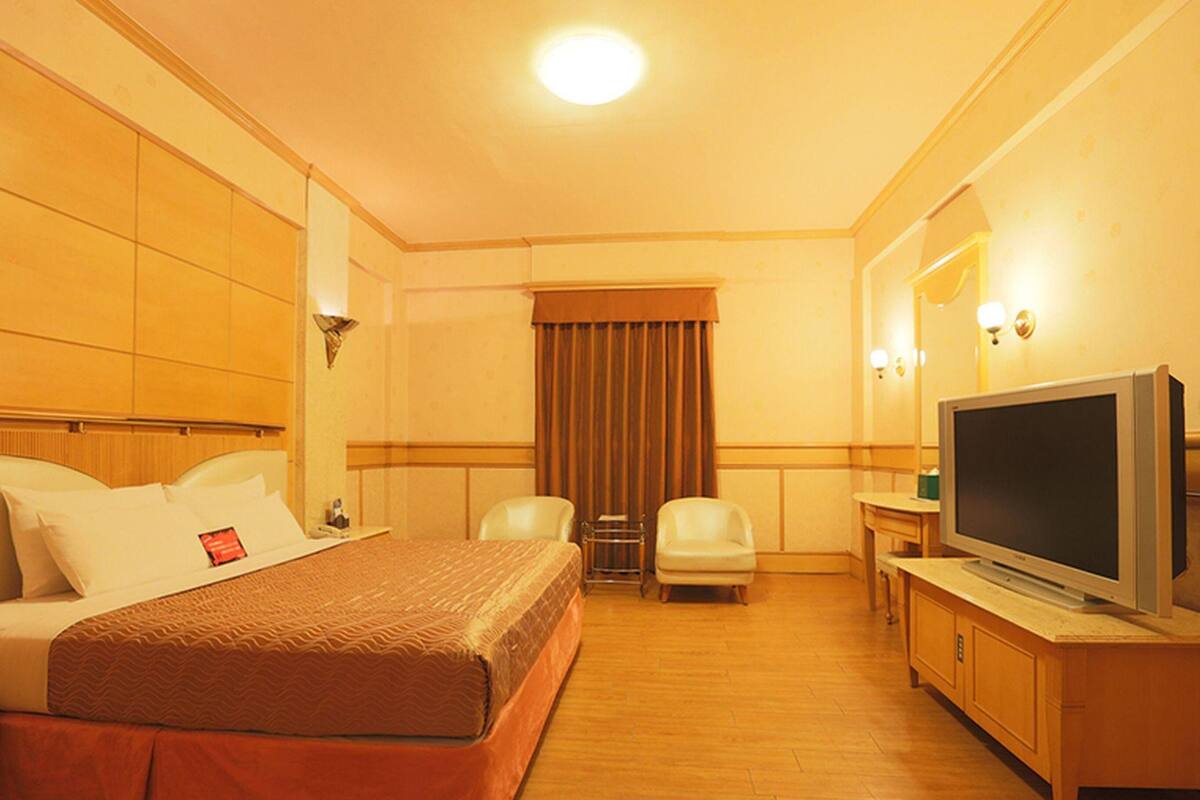 A hotel room with a bed, two chairs, a television, and a window with curtains.