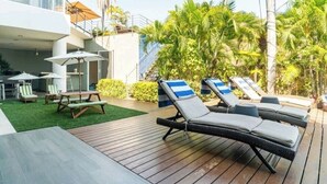 Un espace aménagé au bord de la piscine, avec des chaises longues, une table de pique-nique et un escalier menant à un niveau supérieur.