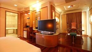 Una habitación de hotel con una cama, un televisor en un mueble de madera, un escritorio con una silla y un baño visible a través de una puerta abierta.