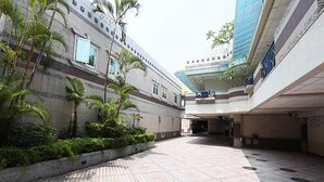 Un patio amplio con suelo de baldosas, palmeras y un edificio moderno con fachada de vidrio.