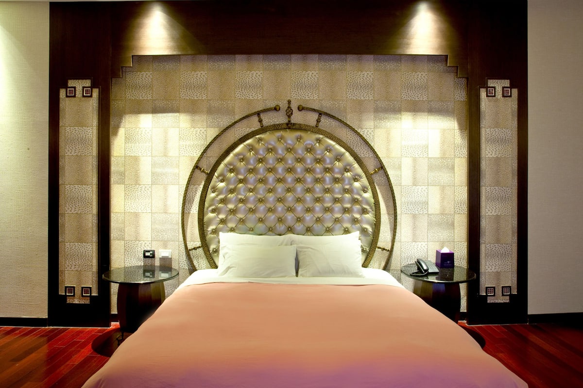 Ein Hotelzimmer mit einem großen Bett, einem runden Kopfteil, zwei Nachttischen und einer Wand mit Muster.