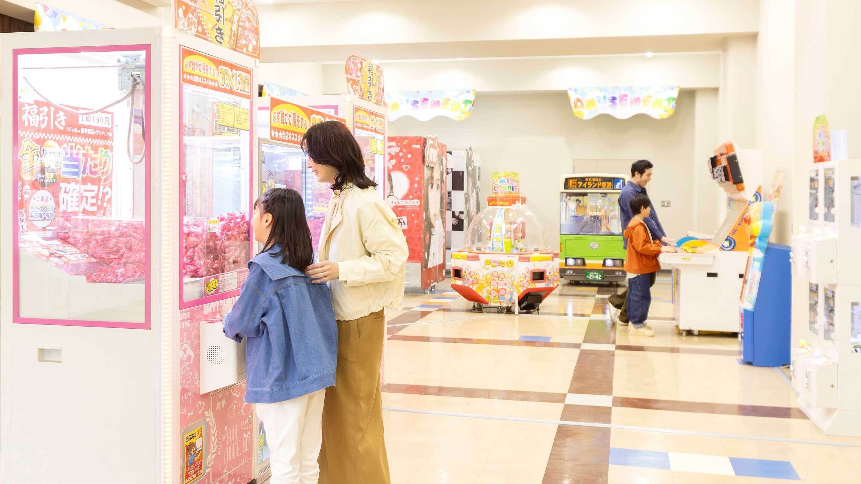 A brightly lit indoor arcade with claw machines and a bus in the background.