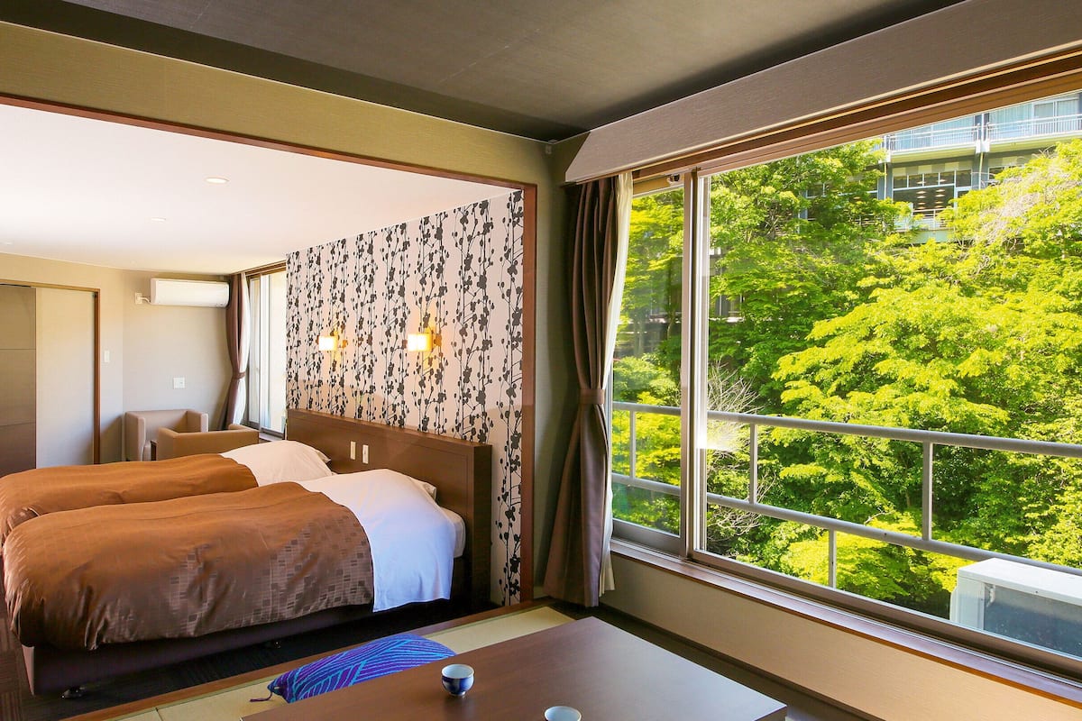 Ett hotellrum med två sängar, utsikt över grönområden och en skjutdörr som leder till ett annat rum.